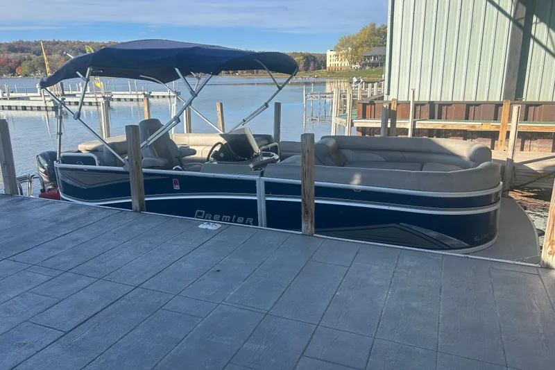 Slide: The Image of 2019 Premier 240 SunSation pontoon boat with Mercury outboard motor, docked near green buildings. - 7