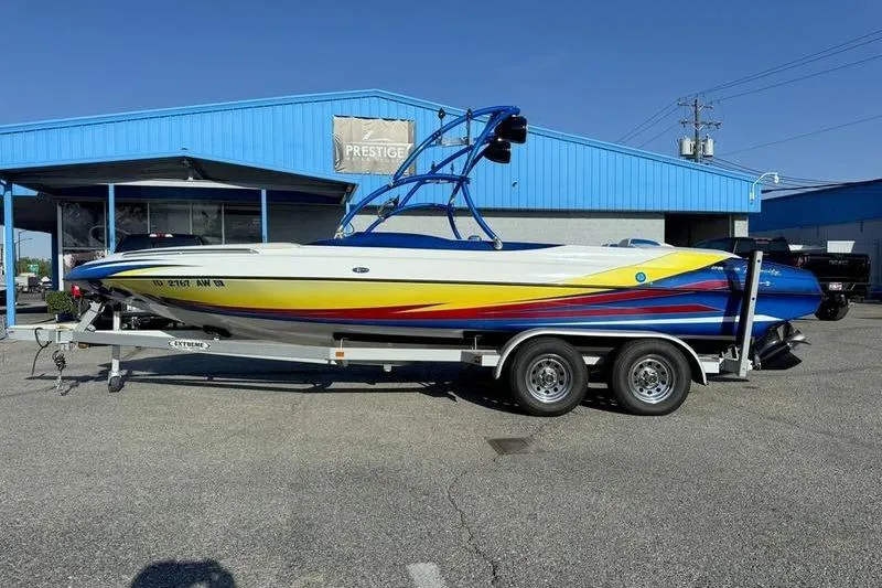 Slide: The Image of 2013 Caliber 1 230 Velocity boat on trailer, parked outside blue building. - 0