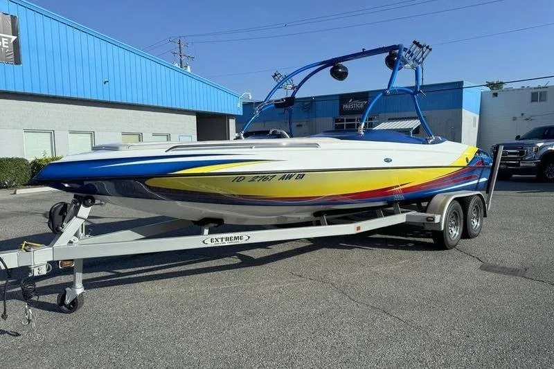 Slide: The Image of 2013 Caliber 1 230 Velocity boat on trailer, vibrant colors, parked outside blue building. - 4
