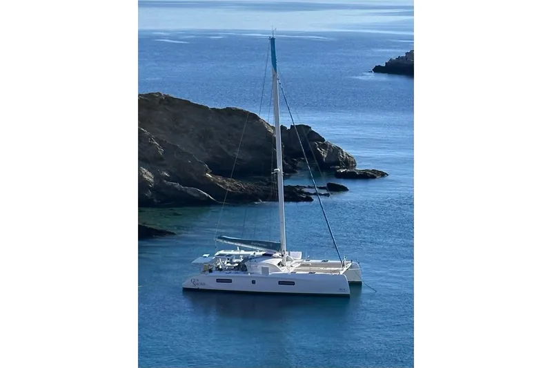 The Image of 2021 Outremer 51 catamaran anchored in serene blue waters near rocky coastline. - 0