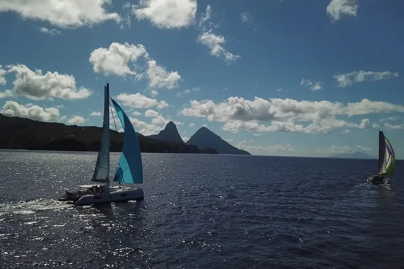 Slide: The Image of Sailboats on the ocean near mountains, featuring a 2021 Outremer 51 catamaran. - 30