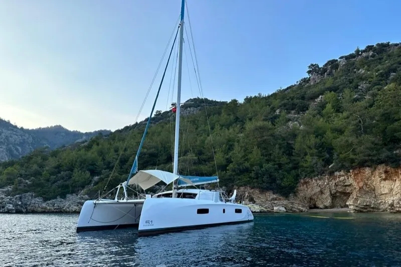 Slide: The Image of 2021 Outremer 51 catamaran anchored in a scenic bay with lush green hills. - 7
