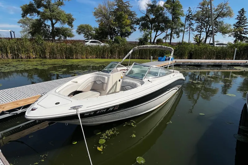 The Image of 2003 Sea Ray 240 Bow Rider boat docked on a calm lake with lush greenery. - 1