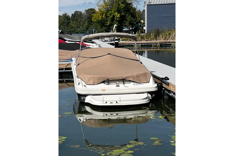 Slide: The Image of 2003 Sea Ray 240 Bow Rider boat docked with cover, surrounded by calm water and greenery. - 4