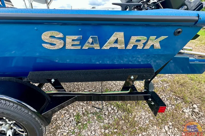 Slide: The Image of 2026 SeaArk C1074 Shadow 18TCC boat, blue exterior, on a trailer, parked on gravel. - 5