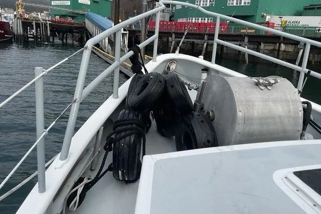 Slide: The Image of Bow of 2006 Custom Sprague boat with tires and equipment, docked near green buildings. - 11