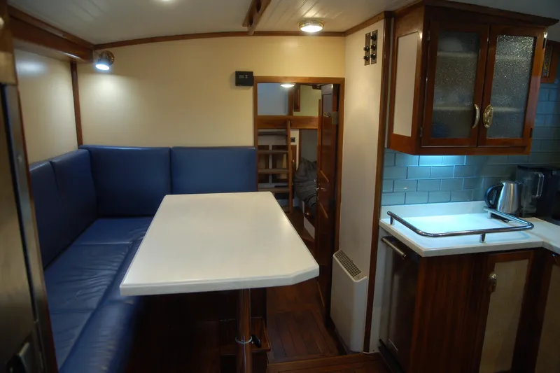 Slide: The Image of Cozy 2006 Custom Sprague boat interior with blue seating, dining table, and kitchenette. - 49