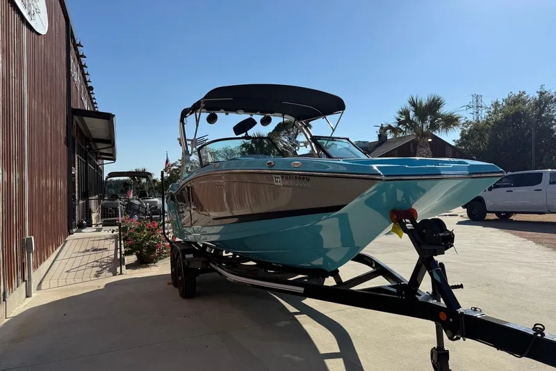Slide: The Image of 2018 MasterCraft NXT22 boat on trailer, parked outdoors near a building. - 2