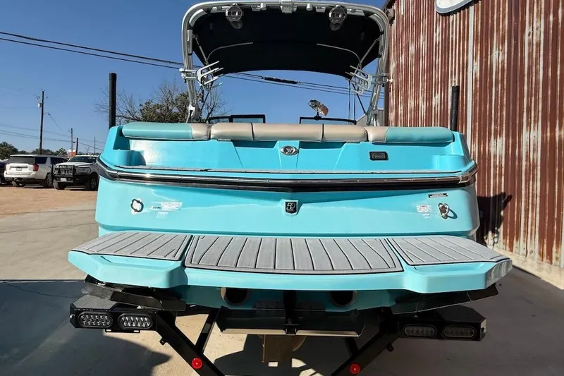 Slide: The Image of 2018 MasterCraft NXT22 boat, turquoise rear view, parked outdoors near a rustic building. - 3