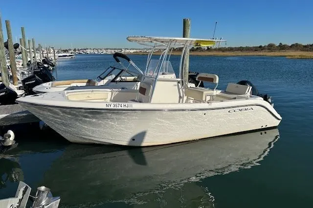 The Image of 2023 Cobia 220DC boat docked in a marina under clear blue skies. - 0