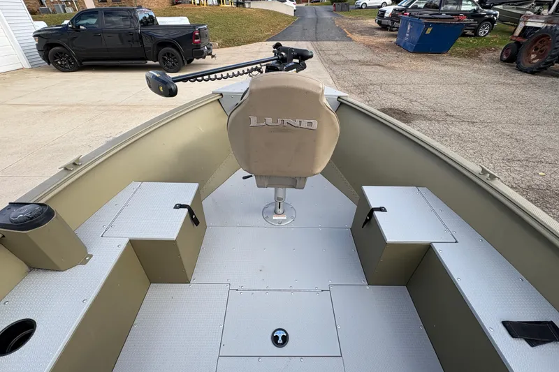 Slide: The Image of 2022 Lund 1800 Alaskan Tiller boat interior with seating and steering, parked outdoors. - 10