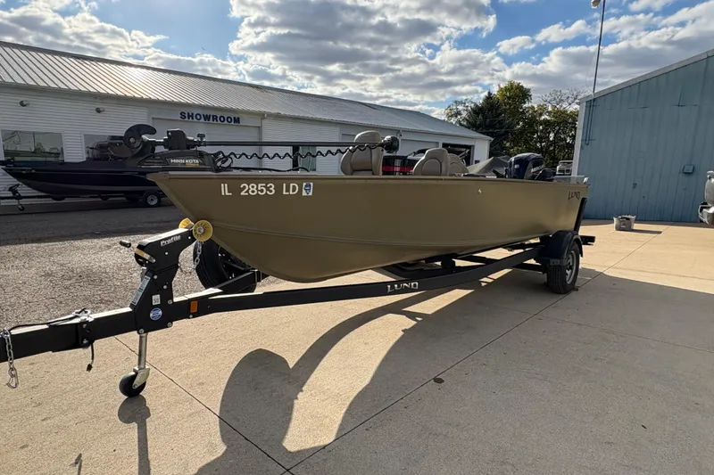 Slide: The Image of 2022 Lund 1800 Alaskan Tiller boat on trailer outside showroom under cloudy sky. - 5