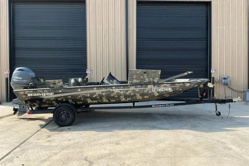The Image of 2015 Ranger RT188 boat with camouflage design on a trailer, parked outside a building. - 0