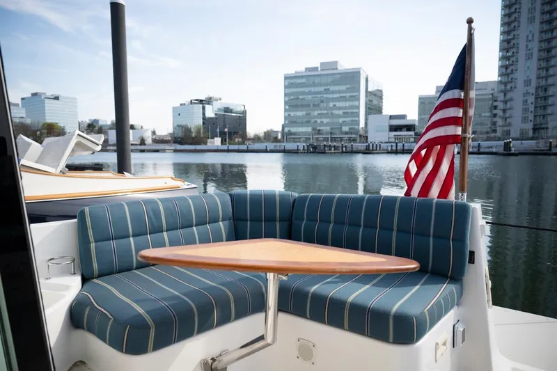 Slide: The Image of 2014 Back Cove 37 yacht with striped seating and American flag, docked near modern buildings. - 28