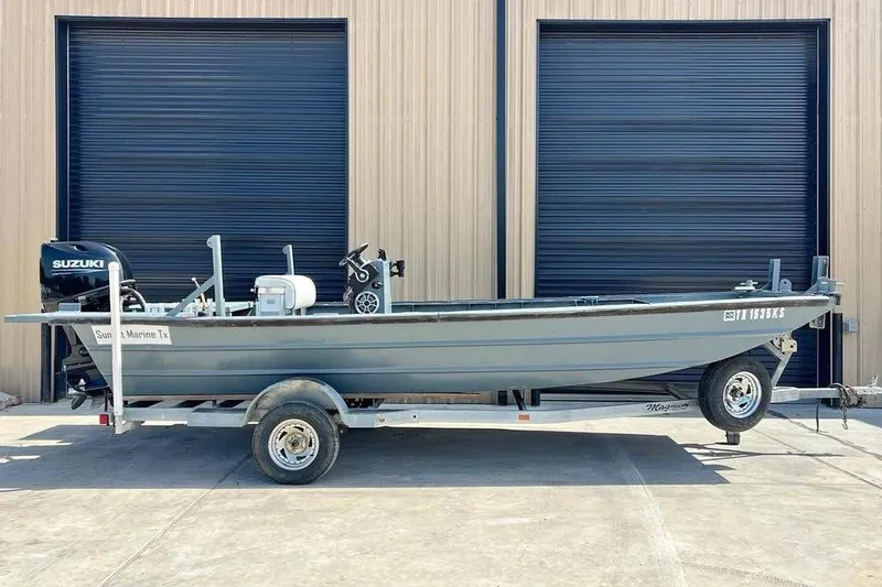 The Image of 1999 Aluminum Boat on trailer with Suzuki outboard motor, parked outside industrial building. - 0