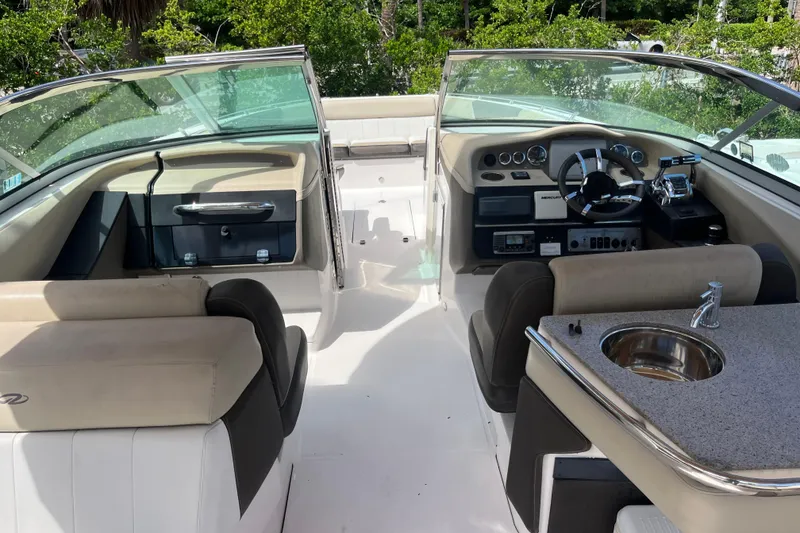 Slide: The Image of 2014 Regal 3200 Bowrider interior with helm, seating, and sink, surrounded by lush greenery. - 6