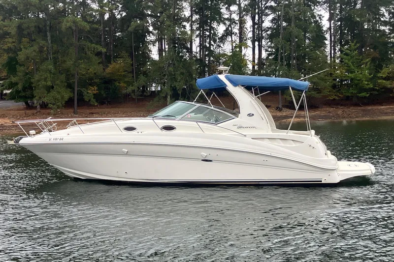 The Image of 2004 Sea Ray 320 Sundancer boat on calm water with forested shoreline. - 0
