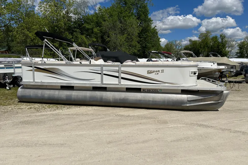 The Image of 2003 Crest 25 II LM pontoon boat parked on gravel, surrounded by trees and other boats. - 0