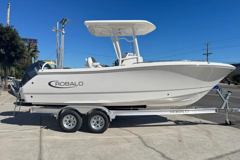 The Image of 2026 Robalo R230 Center Console boat on trailer, parked outdoors under clear blue sky. - 2