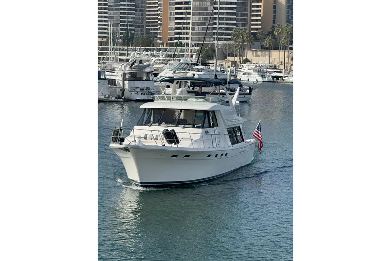 The Image of 1998 Bayliner 4788 Pilot House Motoryacht cruising in a marina, surrounded by other boats. - 0