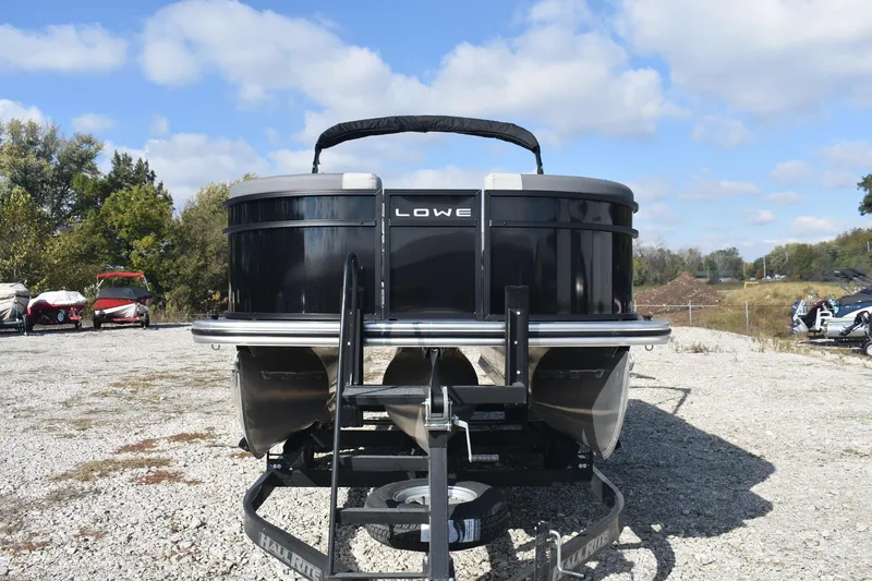 Slide: The Image of 2026 Lowe LS 210 pontoon boat on trailer, parked outdoors under a blue sky. - 1