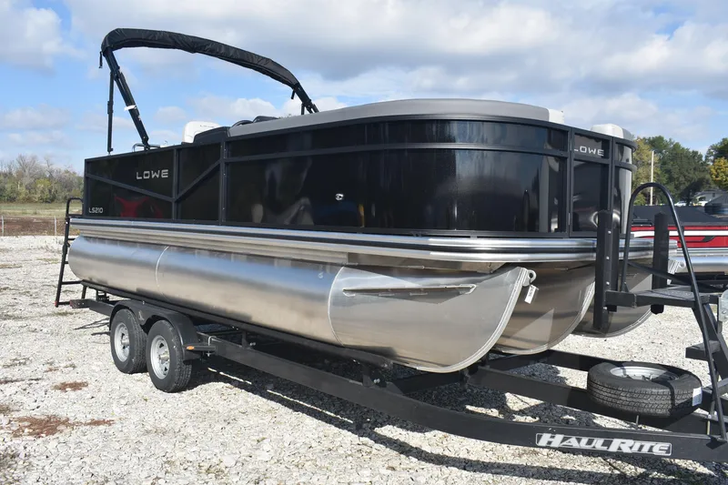 Slide: The Image of 2026 Lowe LS 210 pontoon boat on Haul-Rite trailer, parked on gravel lot. - 7