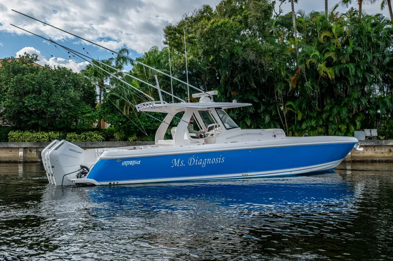 Slide: The Image of 2020 Intrepid 407 Panacea boat, blue hull, docked on calm water, lush greenery background. - 39
