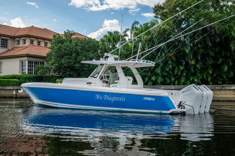 Slide: The Image of 2020 Intrepid 407 Panacea boat, blue hull, docked near waterfront home, lush greenery background. - 44