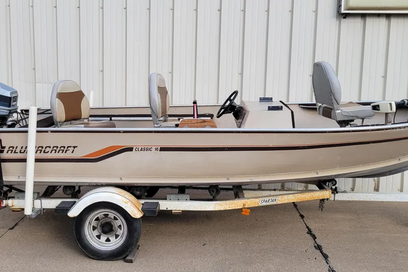 Slide: The Image of 1987 Alumacraft Classic 165 CS boat on trailer, beige with brown accents, parked outdoors. - 14
