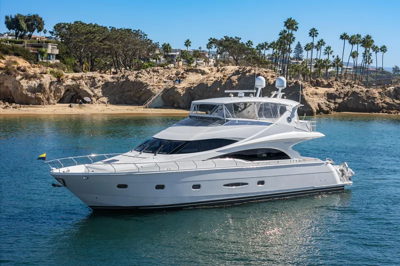 The Image of Luxury 2005 Marquis 65 yacht cruising near rocky coastline with palm trees. - 0