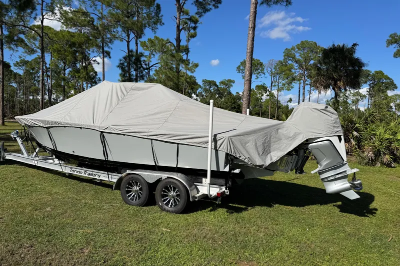 Slide: The Image of Covered 2025 Latitude Tournament Boats 25 on trailer, parked on grass with trees in background. - 34