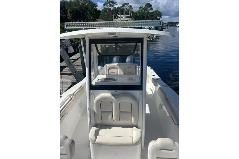Slide: The Image of 2019 Sea Hunt Gamefish 27 boat with white seating, docked by a calm waterway. - 9