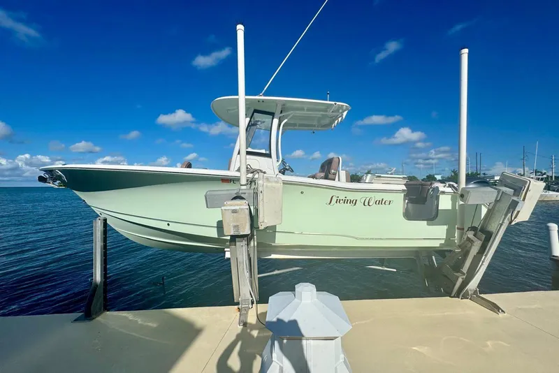 Slide: The Image of 2019 Sea Hunt Ultra 275 SE boat on lift, docked by the ocean under clear blue sky. - 12