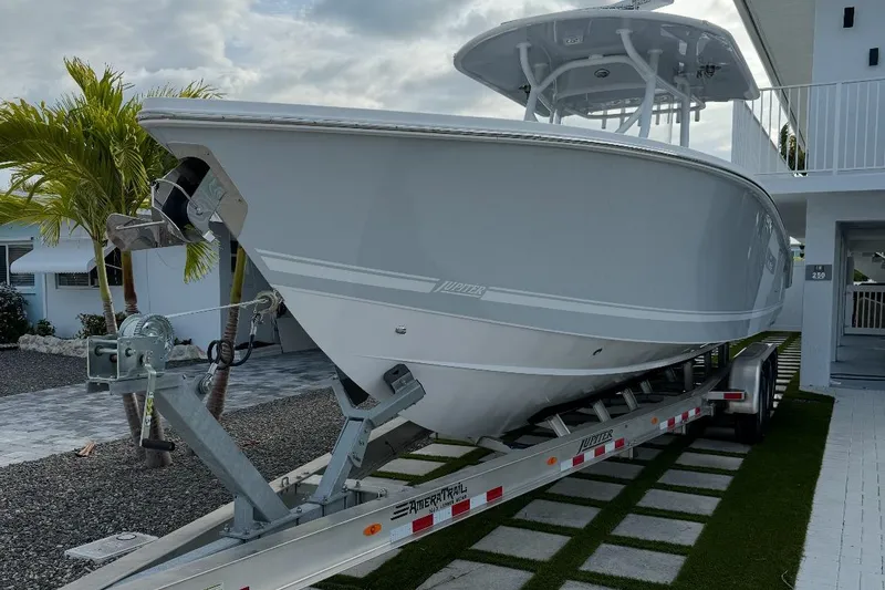 Slide: The Image of 2023 Jupiter 32 boat on trailer, parked near a modern house with palm trees. - 22