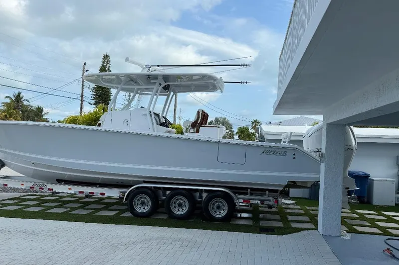 Slide: The Image of 2023 Jupiter 32 boat on trailer in driveway, under cloudy sky. - 23