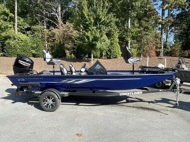 The Image of 2023 Crestliner XFC 179 boat on trailer, parked outdoors, surrounded by trees. - 1