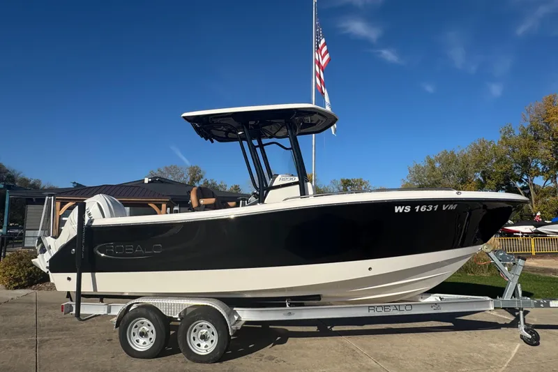 Slide: The Image of 2024 Robalo R230 Center Console boat on trailer, parked outdoors under clear blue sky. - 4