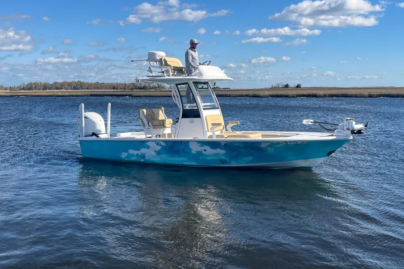 The Image of 2024 Sportsman Masters 247OE Bay Boat cruising on a calm waterway under a blue sky. - 0