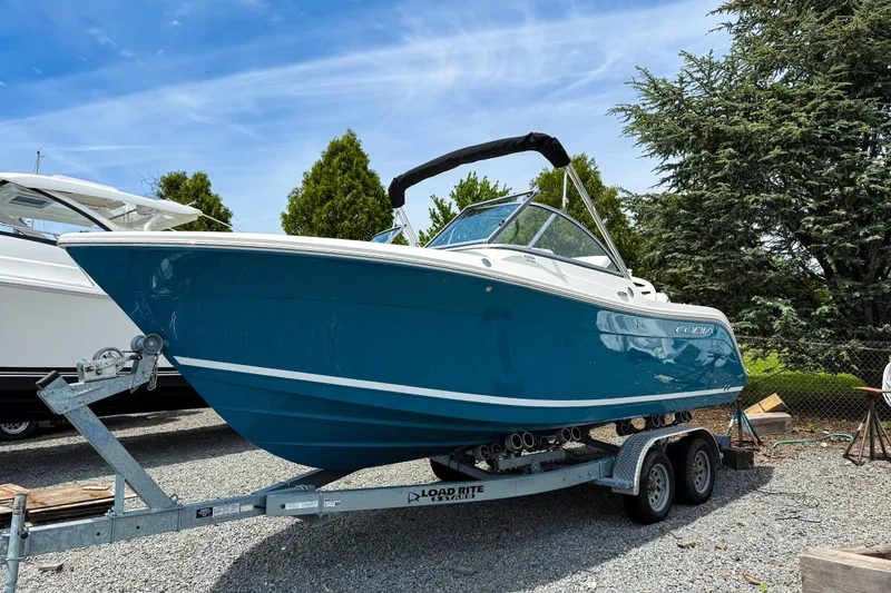 The Image of 2025 Cobia 220 Dual Console boat on trailer, parked outdoors under blue sky. - 0