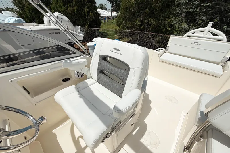 Slide: The Image of 2025 Cobia 220 Dual Console boat interior with white seating and steering wheel. - 10
