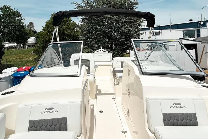 Slide: The Image of 2025 Cobia 220 Dual Console boat with open seating and windshield, docked outdoors. - 21