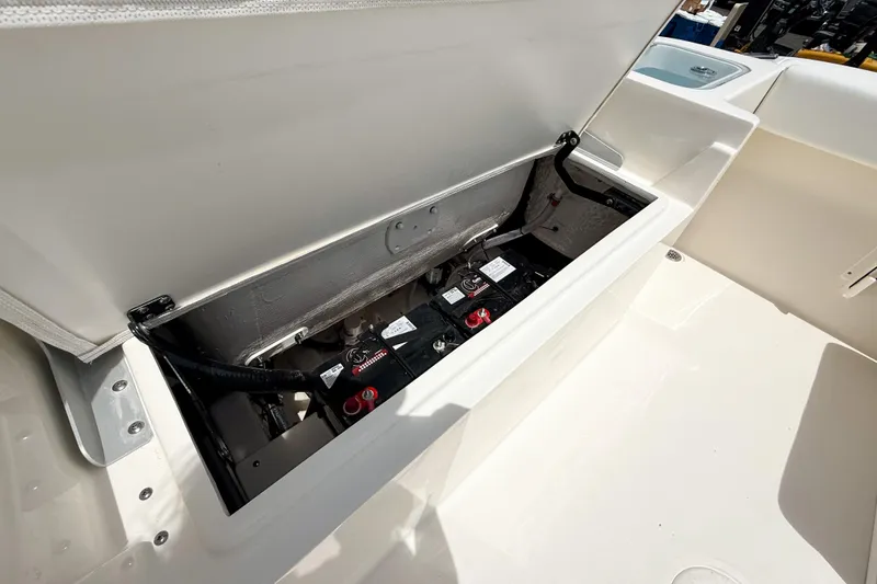 Slide: The Image of 2025 Cobia 220 Dual Console boat battery compartment open, showing battery setup. - 23