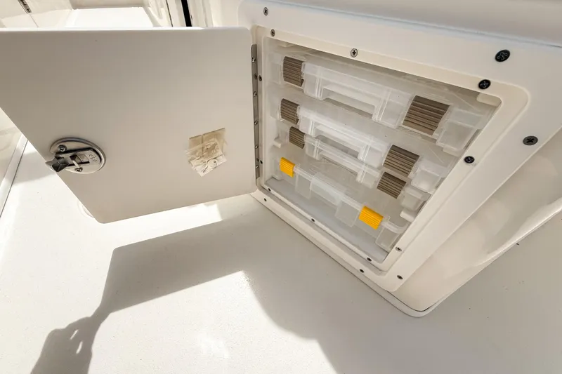Slide: The Image of Open storage compartment on 2025 Cobia 220 Dual Console boat, featuring organized tackle boxes. - 8