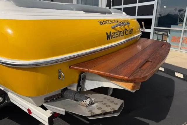 Slide: The Image of Yellow 2002 MasterCraft X30 boat with wooden swim platform, parked near a building. - 10
