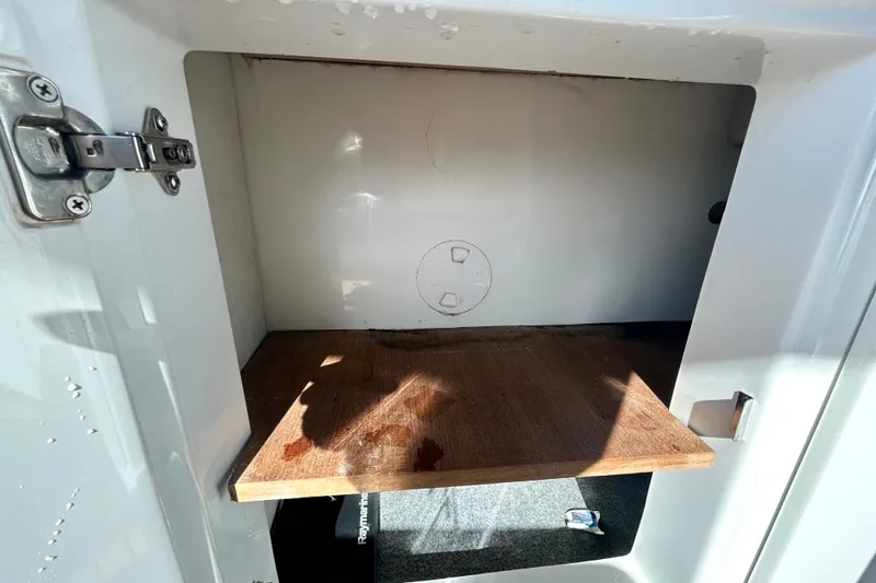 Slide: The Image of Open storage compartment in 2022 Rand Supreme 27 boat, featuring a wooden shelf and metal latch. - 50