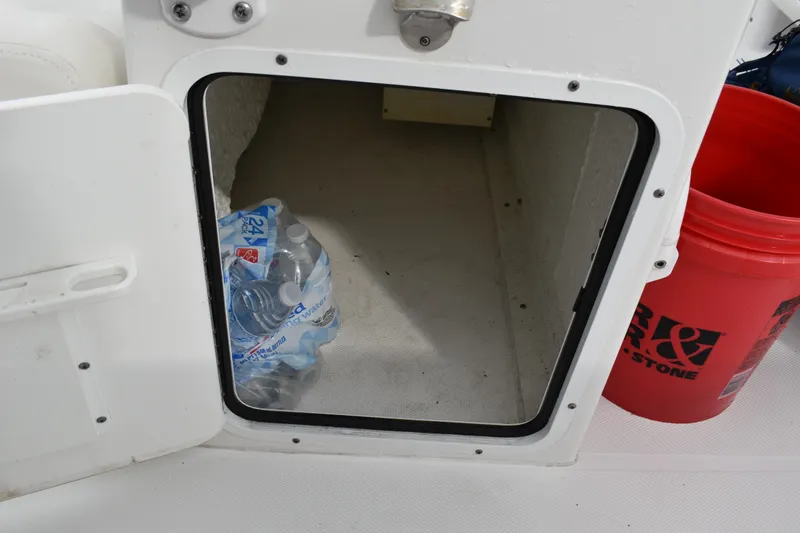 Slide: The Image of Storage compartment on 2023 Sea Hunt Ultra 255 SE boat with water bottles and a red bucket. - 19