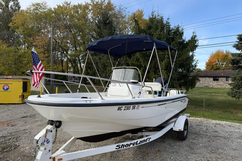 Slide: The Image of 2004 Boston Whaler 160 Dauntless boat on trailer with American flag, parked outdoors. - 0