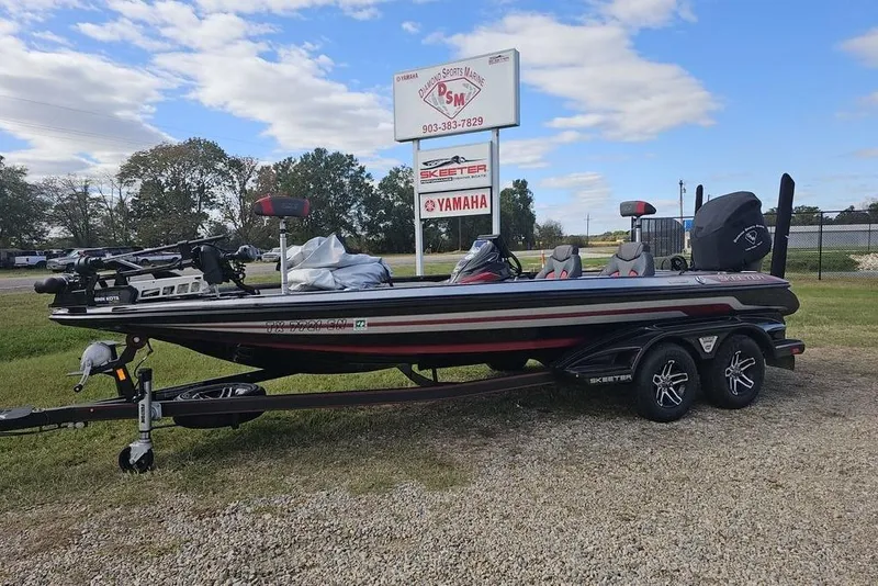 Slide: The Image of 2019 Skeeter FX21 bass boat on trailer, parked near dealership sign under blue sky. - 0