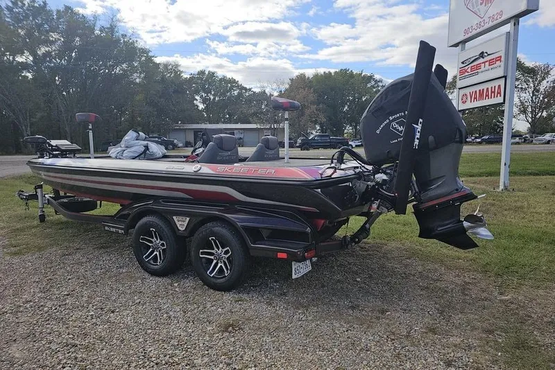 Slide: The Image of 2019 Skeeter FX21 bass boat on trailer, parked outdoors near dealership sign. - 11