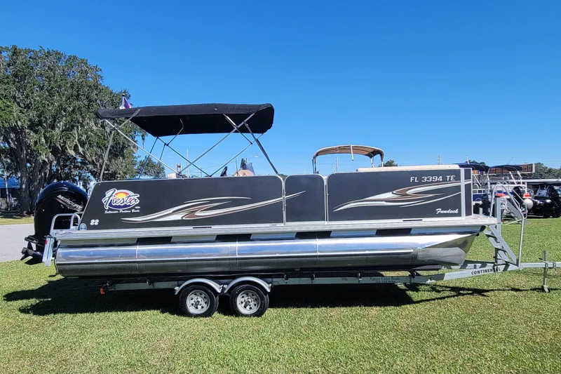 The Image of 2022 Fiesta 22' Fundeck L Sofa RE Deluxe pontoon boat on trailer, parked on grass. - 0
